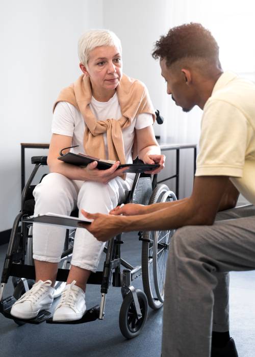 A woman in a wheelchair engaged in a thoughtful conversation with a man, both holding notebooks and discussing, fostering an atmosphere of communication and support.